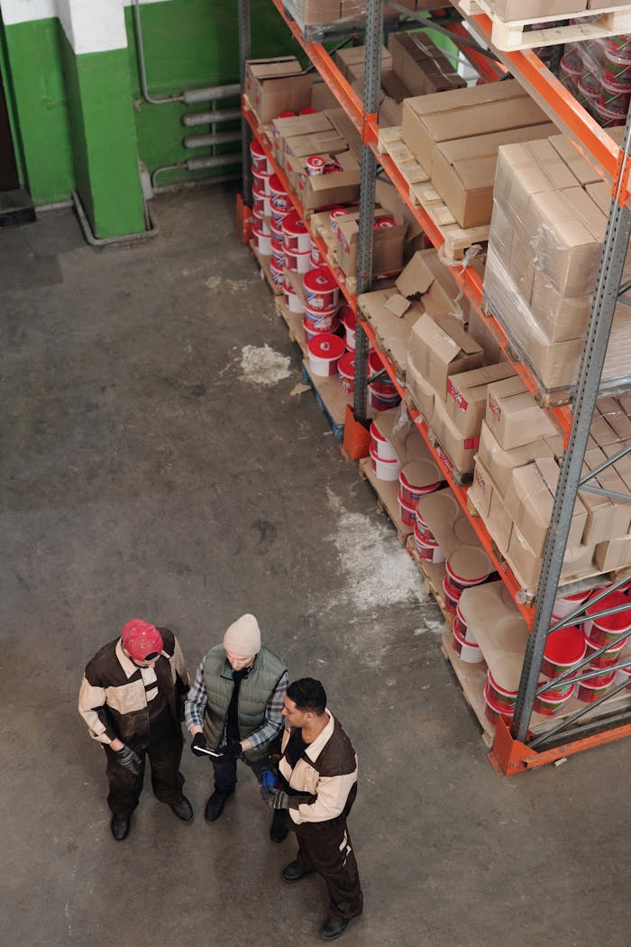 Past Performance Group of warehouse workers discussing logistics and inventory in a large storage area with shelves and packages.